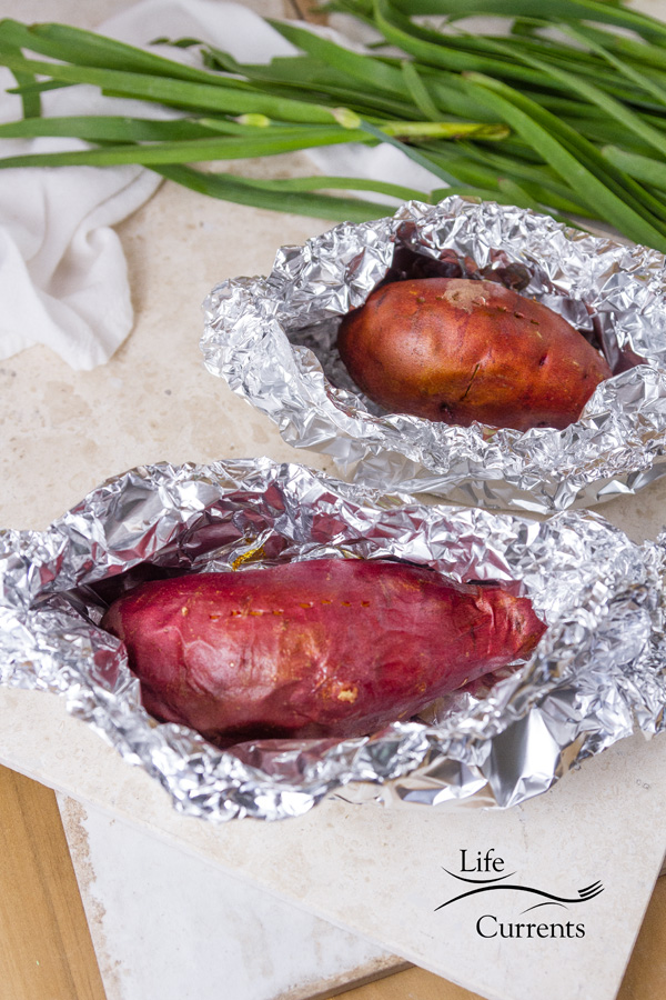Baked sweet potatoes in foil on a white background with chives in the picture