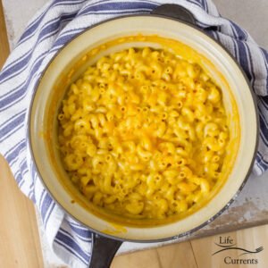 The pot of mac & cheese out of the oven and with a blue striped towel