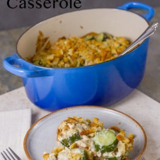 Zucchini Stuffing Casserole in a blue casserole dish with a serving in front on a white plate with a fork and a white napkin on a grey background