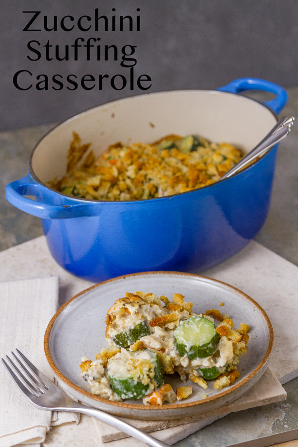 Zucchini Stuffing Casserole in a blue casserole dish with a serving in front on a white plate with a fork and a white napkin on a grey background