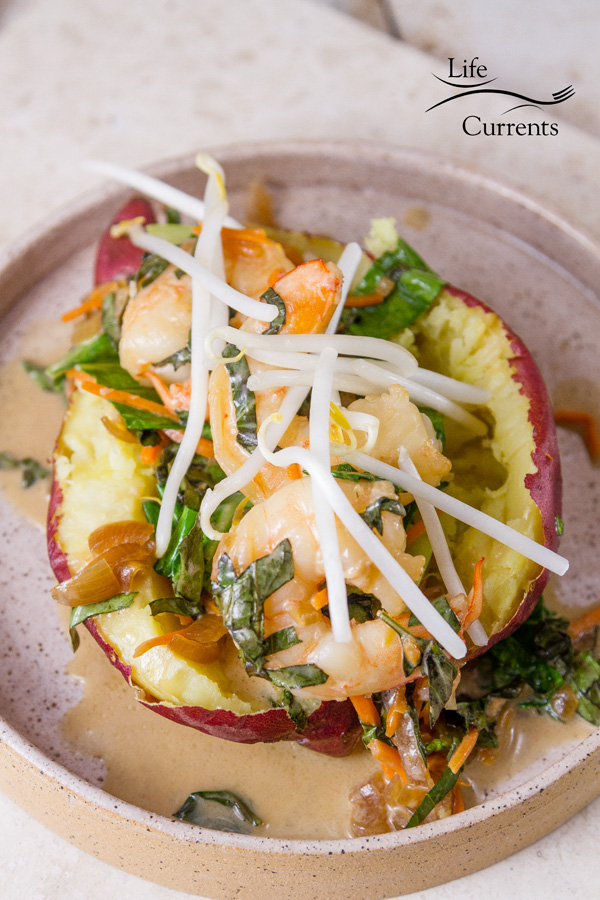 cooked shrimp and veggies stuffed in a sweet potato topped with bean sprouts on a white plate on a white background 