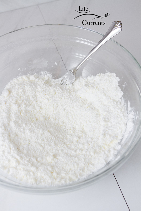 powdered sugar and butter mixed together in a glass bowl with a fork on a white tile background