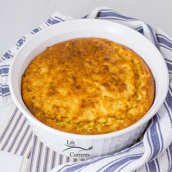 corn casserole baked in a white casserole dish on a blue striped cloth