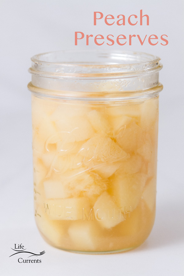 an opened glass mason jar filled with peach preserves on white background with a title
