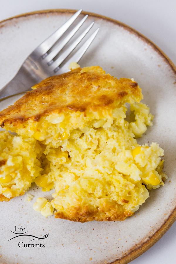 A serving of corn casserole on a white plate with a fork 