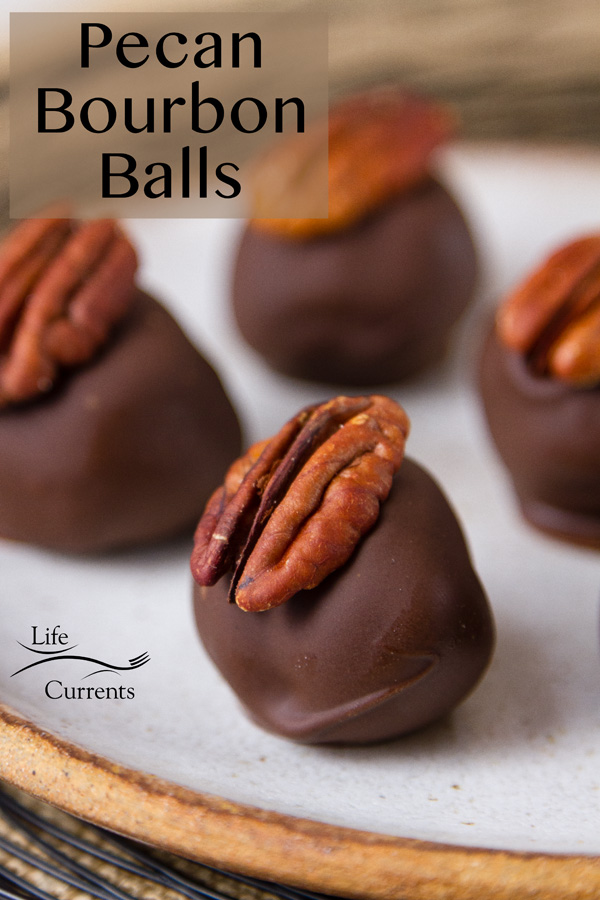 Pecan Bourbon Balls candies with a pecan half on top on a white plate that's set on a black wire plate and the title is on the image 