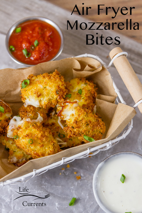 Crispy on the outside, cheesy and ooey gooey on the inside, these Air Fryer Mozzarella Bites are super easy to make and even easier to eat! mozzarella pieces coated in bread crumbs air fried in a wire basket with a brown paper liner served with small aluminium ramekins of marinara sauce and ranch dressing garnished with green onions