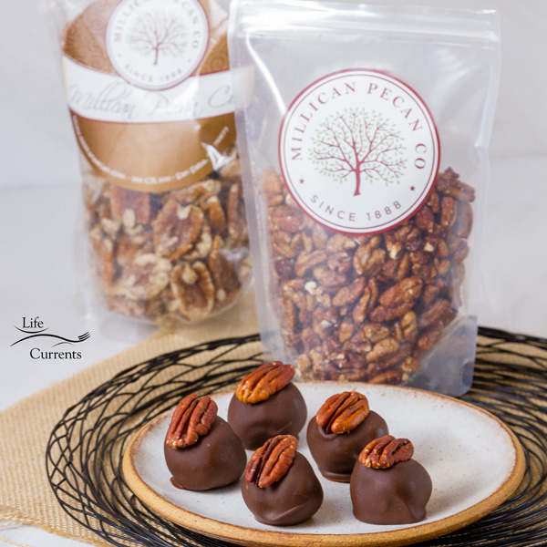 Pecan Bourbon Balls on a white plate in front of bags of pecans from Millican Pecan Company.