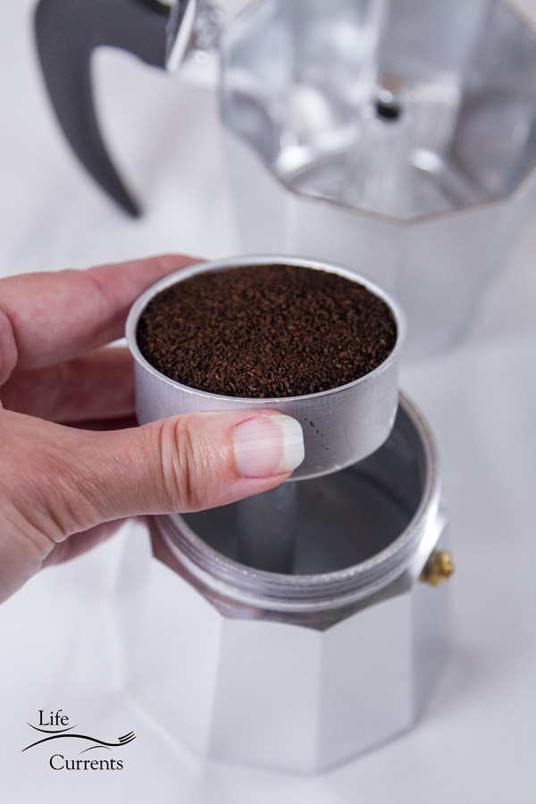 coffee grounds in the well of the stovetop espresso maker, the bottom is filled with water all on a white background