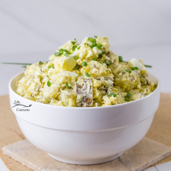 A big white bowl filled with potato salad on a white and brown background