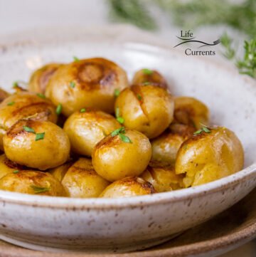cooked potatoes in a white ceramic bowl on a brown platter with rosemary in the background