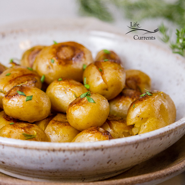 cooked potatoes in a white ceramic bowl on a brown platter with rosemary in the background 