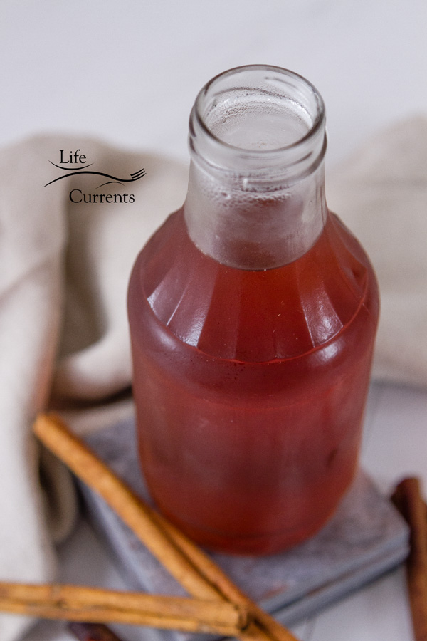 Cinnamon Simple Syrup in a glass jar on grey tiles with cannamon sticks at the bottom and a cloth napkin in the back