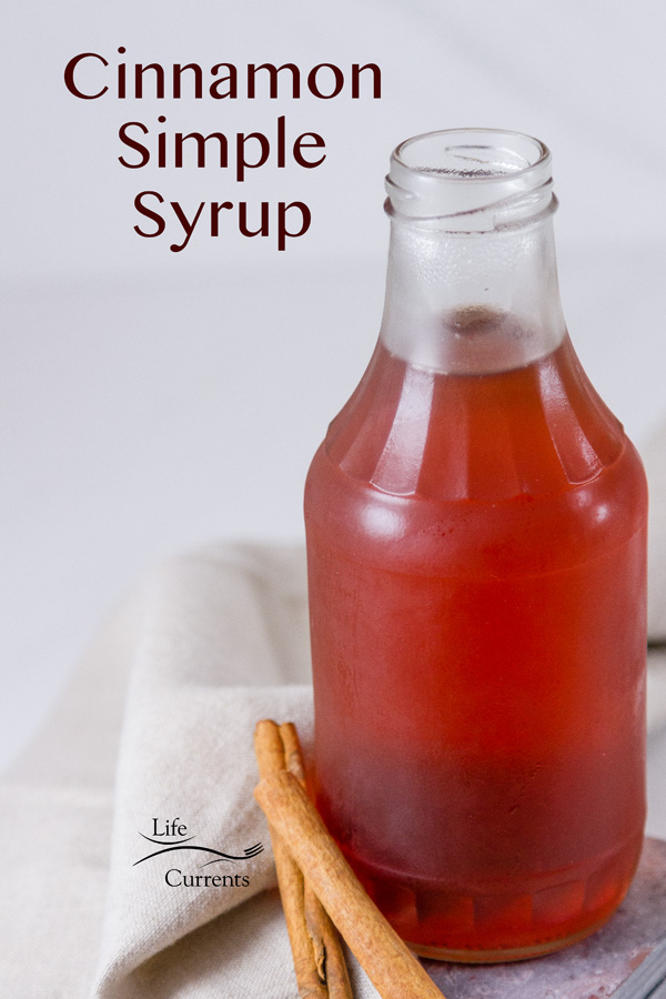 Cinnamon Simple Syrup in a glass jar with cinnamon sticks next to it near a grey cloth napkin on a white background with a title