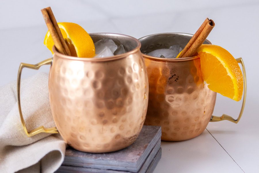 two copper cups garnished with orange slices and cinnamon sticks.