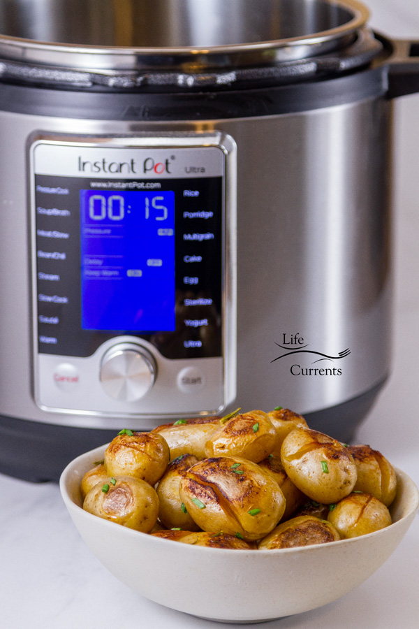 An Instant Pot in the background behind a small white bowl full of cooked potatoes