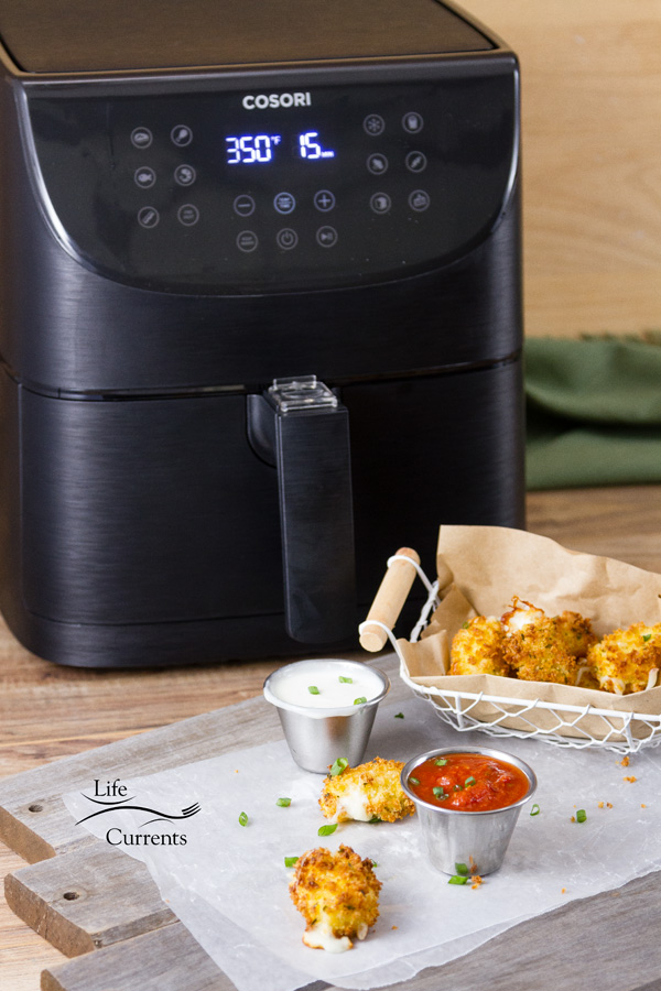 the COSORI 5.8-quart Air Fryer behind the air fryer mozzarella bites served on white parchment paper with ranch and marinara all on a wooden background
