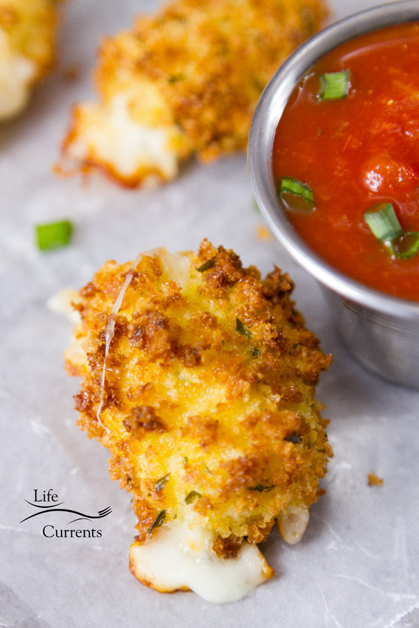 Air Fryer Mozzarella Bites are super easy to make and even easier to eat! Serve them as an appetizer or as a side dish, and since their made in the air fryer they have fewer calories and less fat, and no guilt. These are a must try! Air Fryer Mozzarella Bites on a white waxed paper liner served with a ramekin of marinara sauce and garnished with green onions