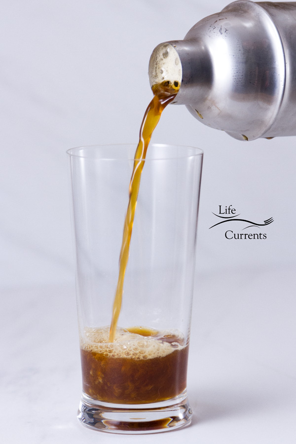 pouring the iced shaken coffee from the cocktail shaker into a glass on a white background