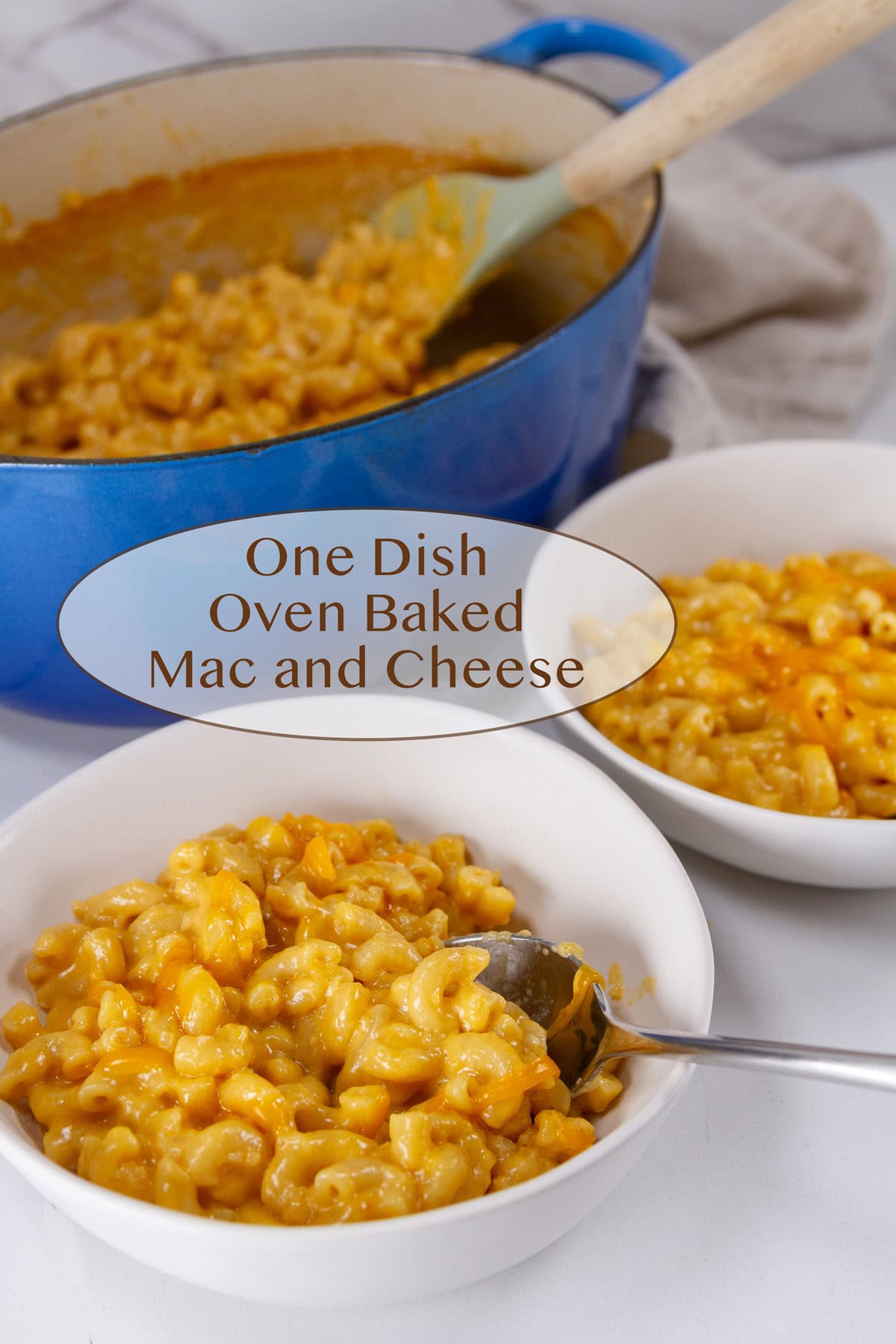 two white serving dishes with bowls of mac & cheese in front of the casserole dish.