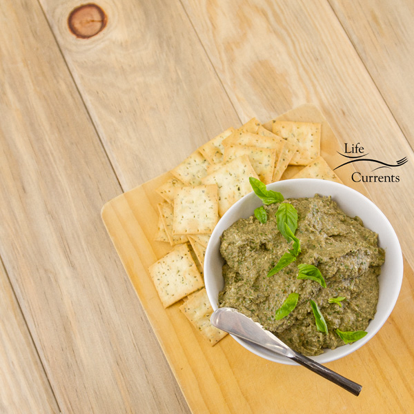 Mushroom Walnut Pesto in a white bowl served on a wooden cutting board with crackers all on a wood background