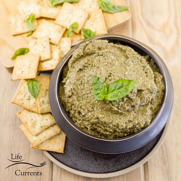 This Mushroom Walnut Pesto Spread in a black bowl on a small black plate with crackers and lots of green basil leaves 