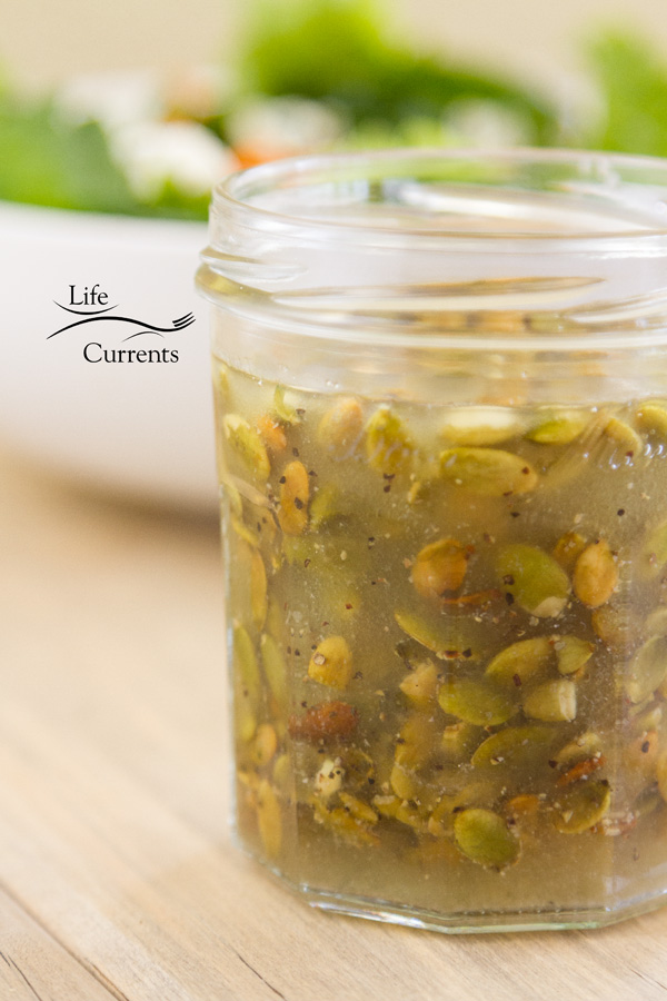 Toasted Pumpkin Seed Vinaigrette in a small glass jar in front of a bowl of salad 