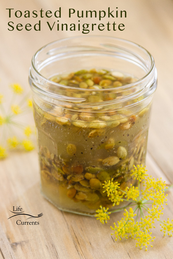 Toasted Pumpkin Seed Vinaigrette in a small glass jar with yellow flawers next to it all on a wood background