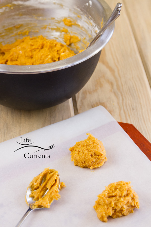 pumpkin cookie dough in a bowl with two cookies scooped out and a spoon with dough on it 
