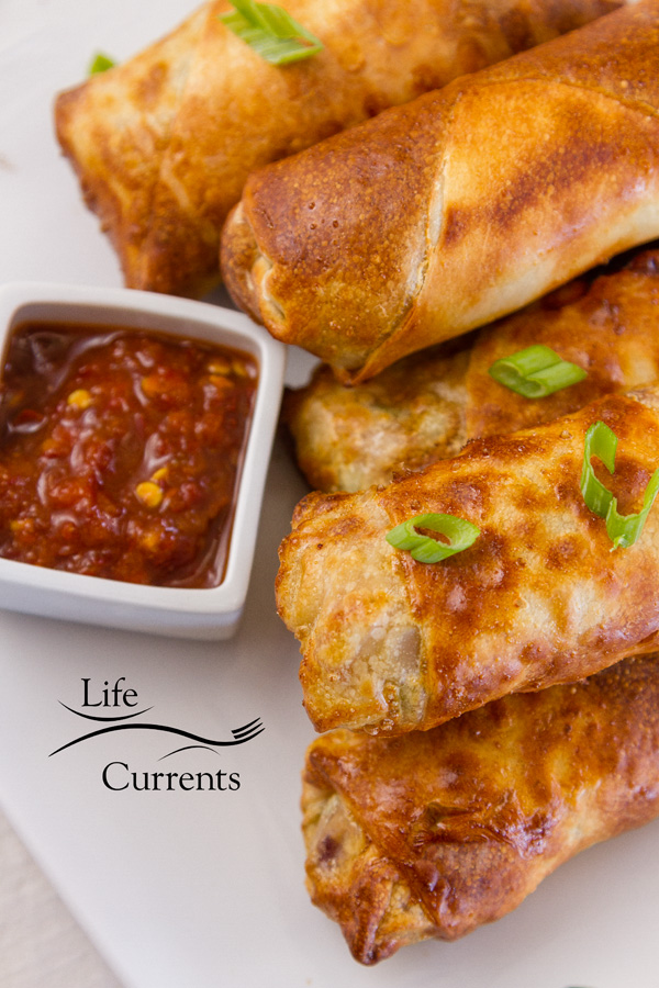Egg rolls stacked on a white plate with chili garlic dipping sauce 