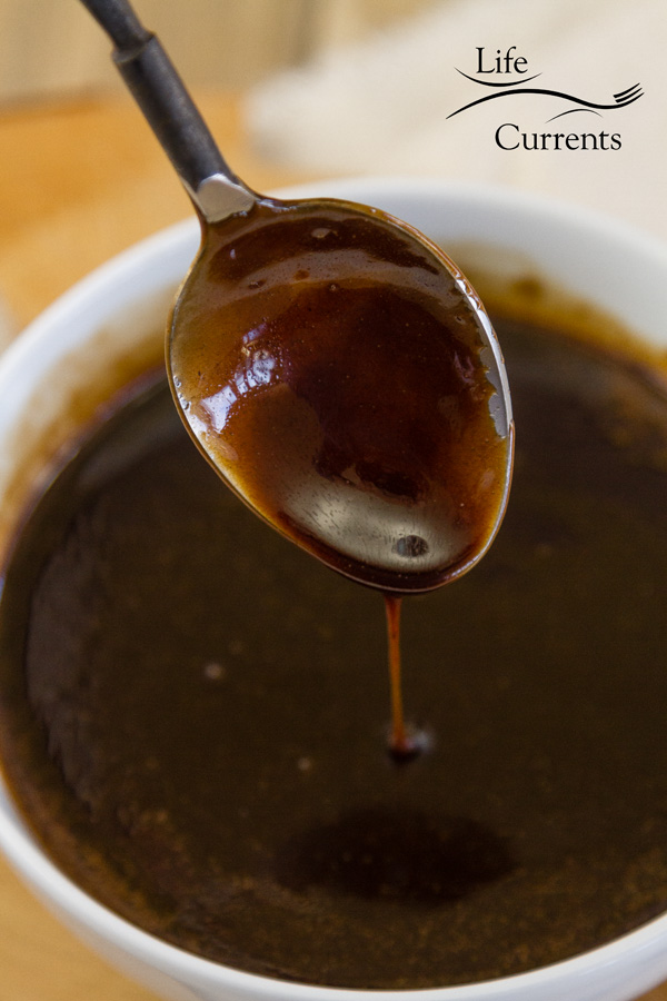 Dark mocha caramel sauce in a white bowl with a spoon drizzling it 