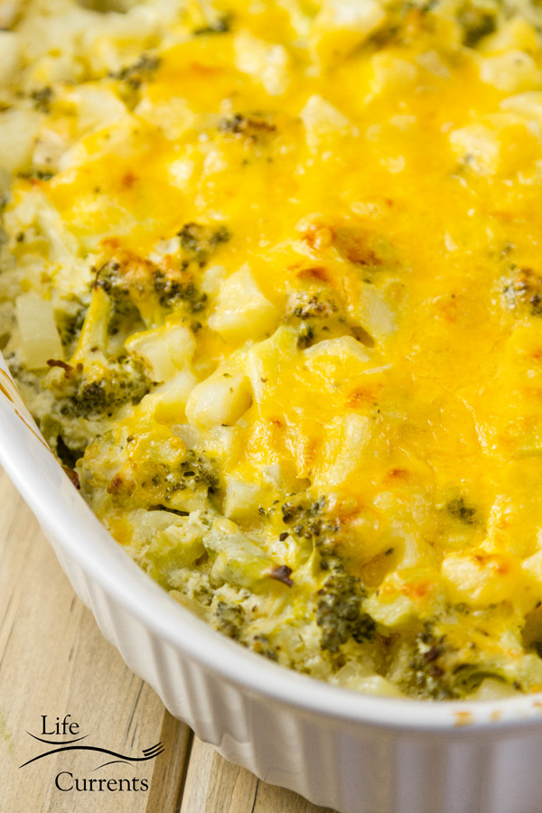 a close up of broccoli potato casserole in a white casserole dish on a wooden background