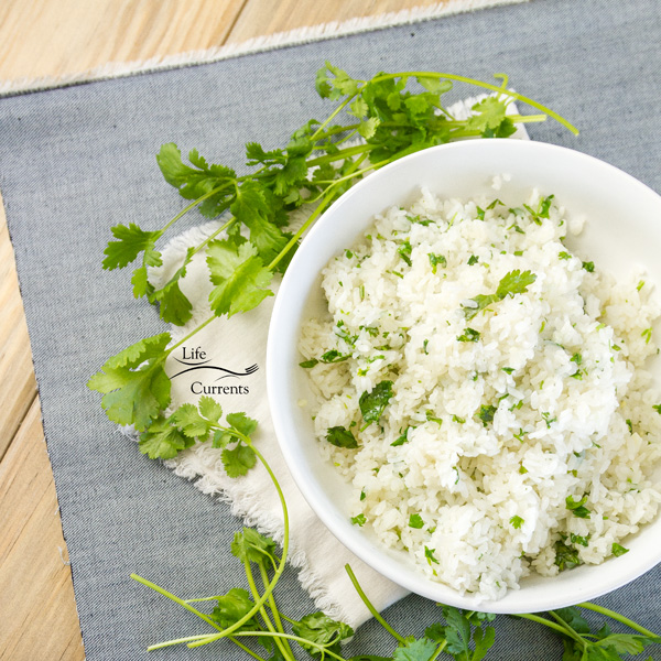 top down view of a white bowl with cilantro rice on a blue cloth with a white napkin and cilantro stems 