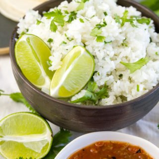 a bowl of cilantro lime rice in a dark brown bowl served with salsa and tortillas on the side