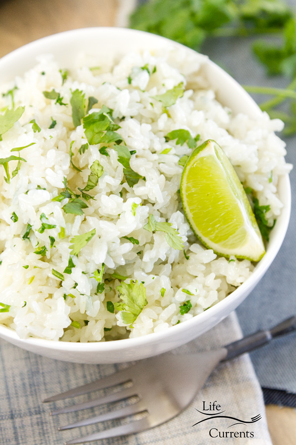 a white bowl filled with cilantro lime rice on a cloth napkin with a fork and a lime wedge 