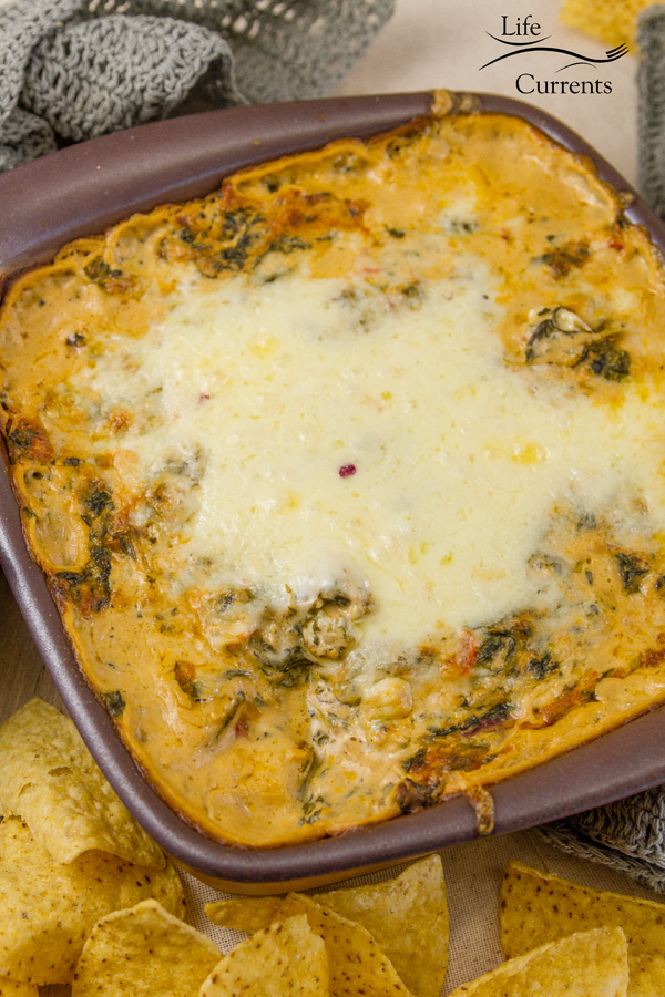 Cheesy Fiesta Spinach Dip - Creamy and cheesy, this hot spinach dip is filled with Mexican flavors, and it’s the perfect addition to any taco bar, tailgate, game day spread, or party! Cheesy Fiesta Spinach Dip will have all your guests asking for the recipe! vertical image of Cheesy Fiesta Spinach Dip with tortilla chips