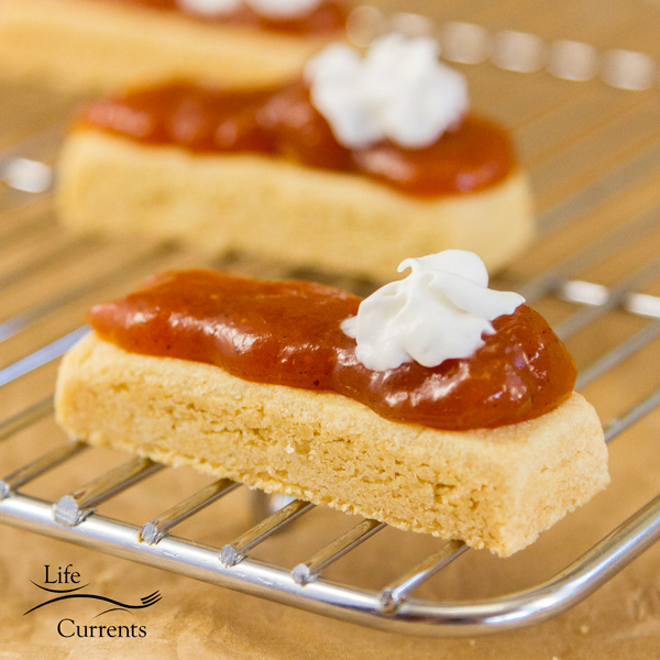 Shortbread cookies topped with pumpkin butter and whipped cream on a cooking rack, square image 