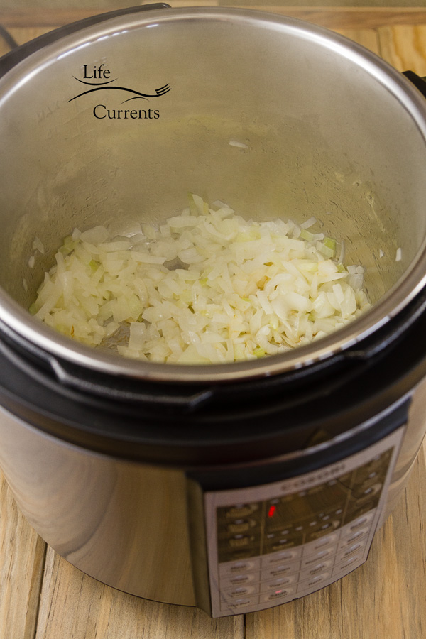 onions sauteing in the insert of a pressure cooker