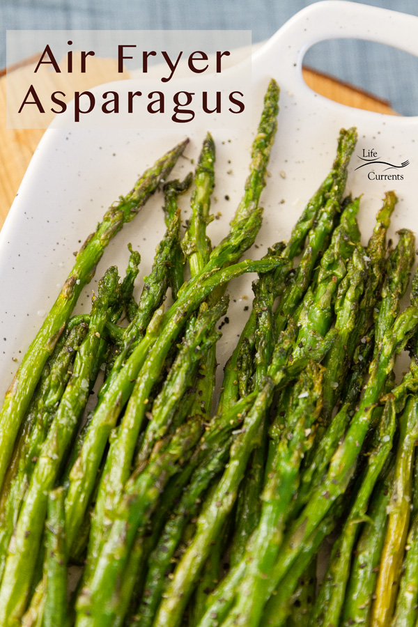 Cooking asparagus in the air fryer requires just 2 simple ingredients (plus salt and pepper), and is ready in a fraction of the time that it would take to oven roast it. This Air Fryer Roasted Asparagus will be your favorite way to cook asparagus from now on! asparagus roasted in the air fryer and served on a white platter with a wood block and a blue napkin in the back
