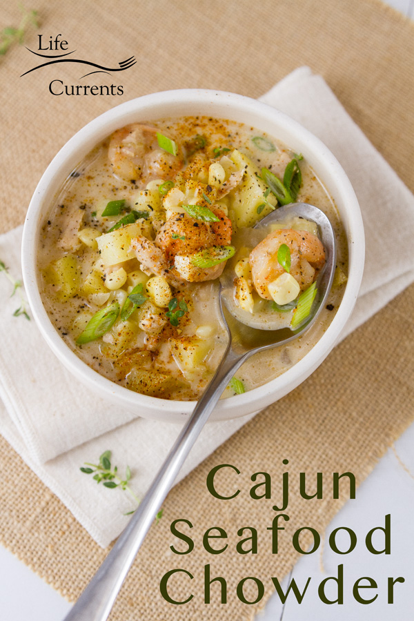 This Cajun Seafood Chowder is rich and creamy, with just the right amount of Cajun spiced seafood including shrimp and tuna, along with sweet corn and earthy potatoes. It’s perfect comfort food that will make you happy all winter long. A bowl of Cajun seafood chowder in a white bowl with shrimp, potatoes, corn, and green onions, and a spoon on a napkin