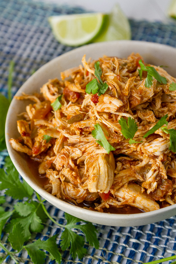 a bowl full of shredded cooked chicken with lime wedges and cilantro