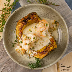 a bowl filled with a cooked acorn squash topped with shrimp in cream sauce.