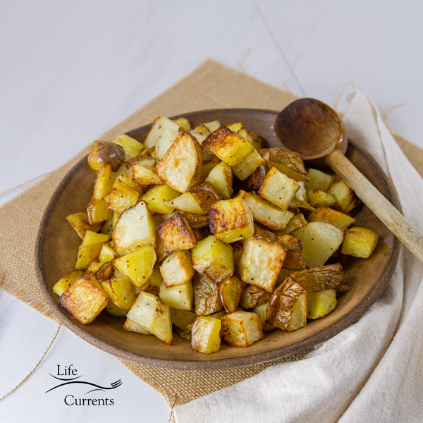 Sheet Pan Roasted Potatoes are an easy, delicious side dish for any meal. This super easy method produces perfectly cooked potatoes that are crispy outside and tender and creamy inside. Square crop of Potatoes in a brown bowl with a spoon
