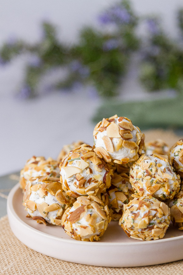 Pepper Jelly Cheese Balls stacked on a plate with rosemary in the background