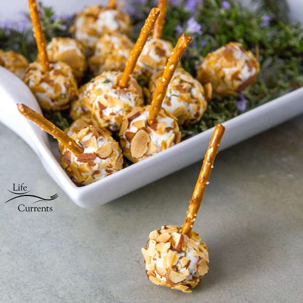 Pepper Jelly Cheese Balls in a serving platter on top of fresh rosemary and one has been taken out and placed in front of the tray