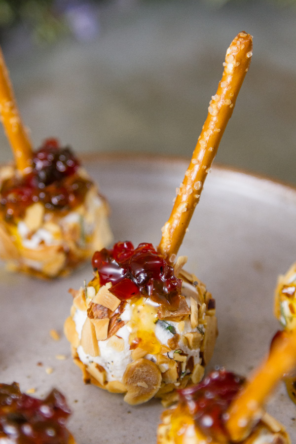 Pepper Jelly Cheese Balls on a plate all topped with more pepper jelly and a pretzel stick handle