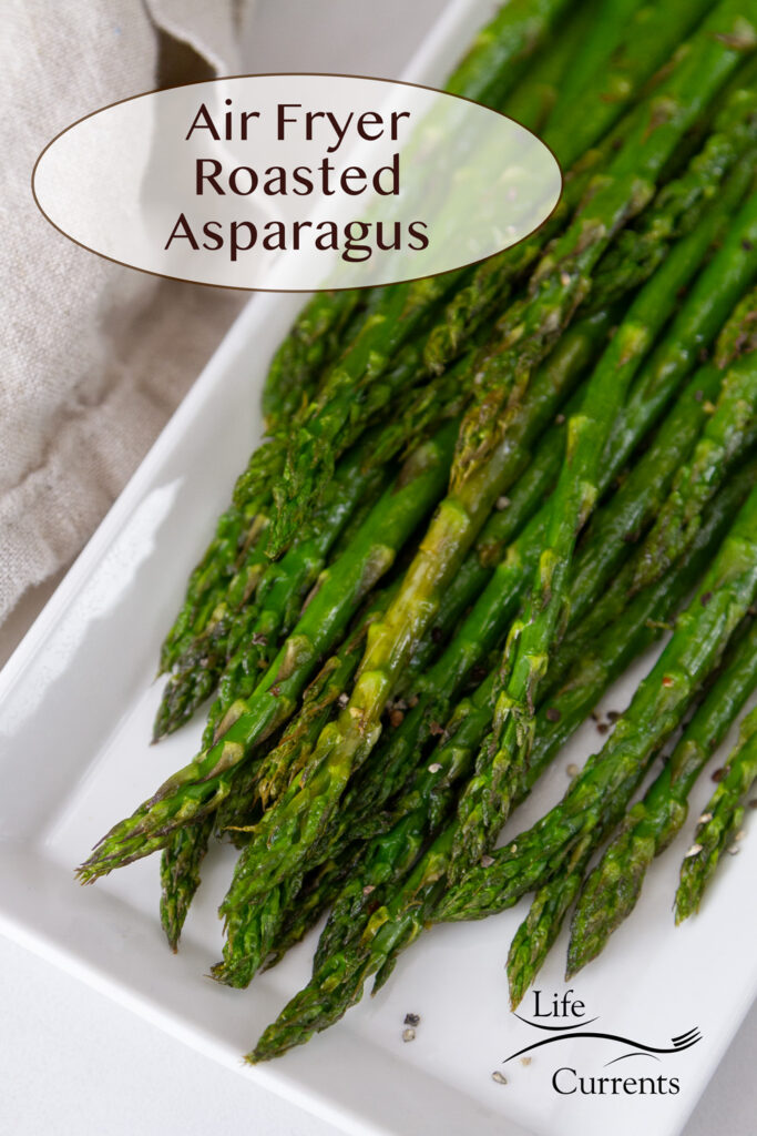 A white plate with freshly cooked asparagus on it, a napkin on the side, title on top: Air Fryer Roasted Asparagus.