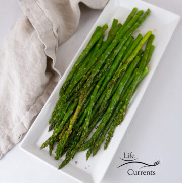 looking down on a plate full of cooked asparagus, a napkin to the side.