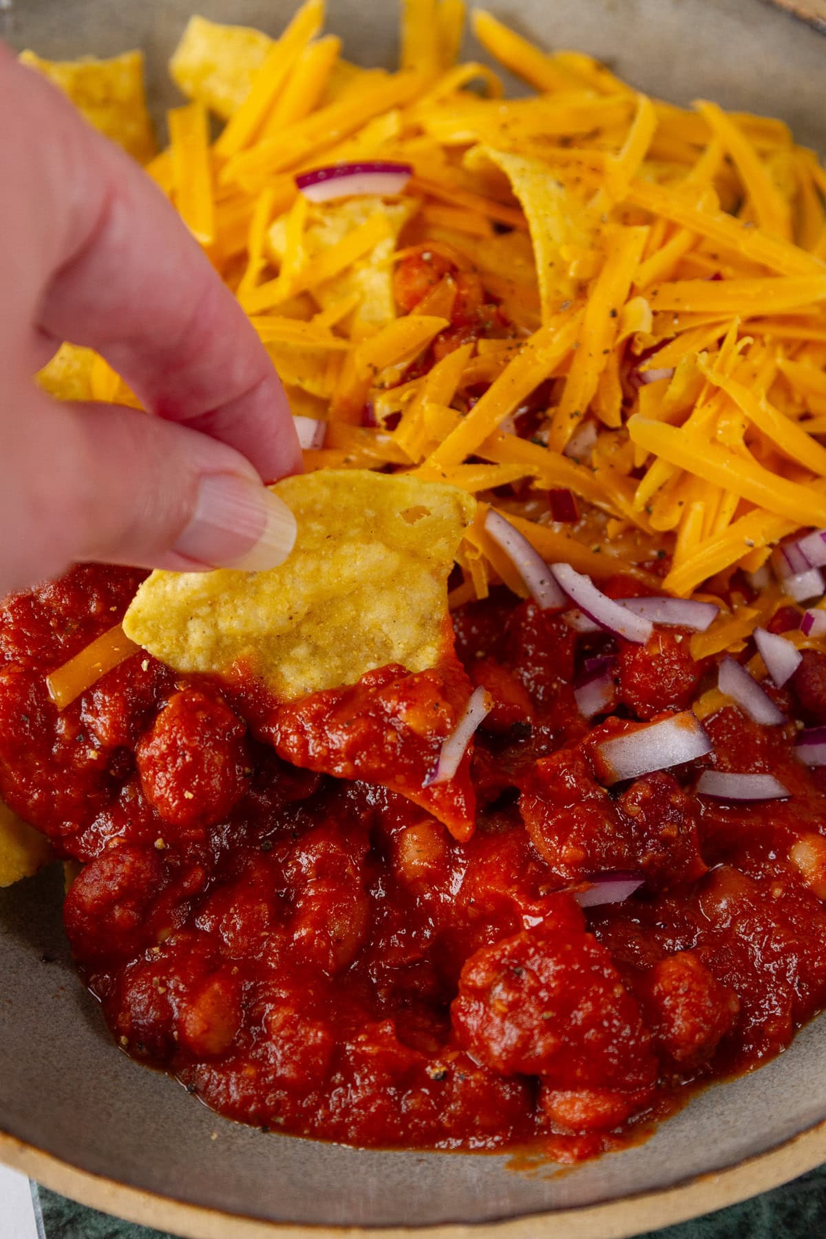 dipping a chip into chili and cheese for chili cheese nachos.
