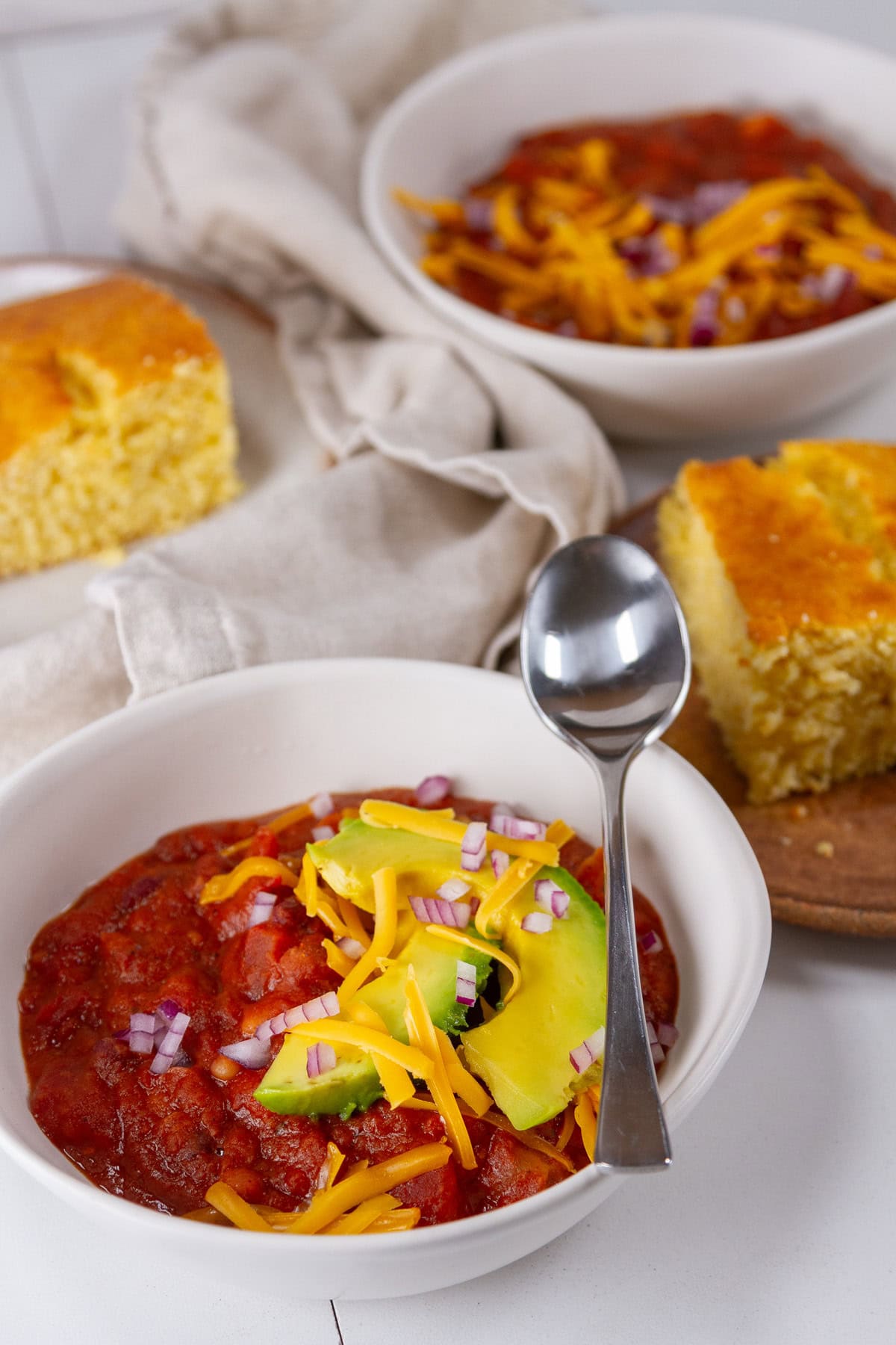 two bowls of chili with cornbread and the chili is topped with avocado, cheese, and onions.
